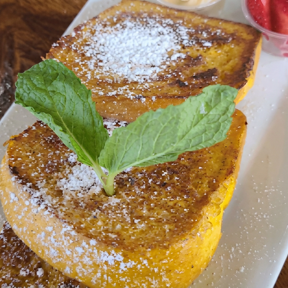 Stacked French toast slices dusted with powdered sugar, garnished with mint, and served with strawberries on a white plate.