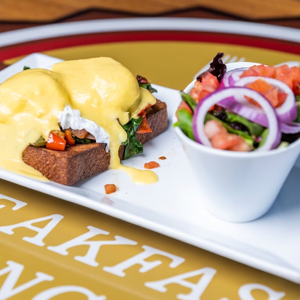 Eggs Benedict with hollandaise sauce on toast, served alongside a fresh salad with tomatoes and red onions.